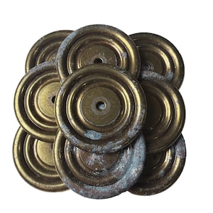 May include: A collection of antique brass hardware components, likely for furniture or decorative use. The circular pieces have a central hole and a raised, concentric ring design. Some show signs of age with a patina of blue-green oxidation.