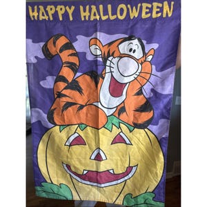 Może przedstawiać: Flaga na Halloween z Tygrysem z Kubusia Puchatka, na uśmiechniętej dyni. Flaga ma fioletowe tło z białymi chmurami i słowami "HAPPY HALLOWEEN" w kolorze żółtym.