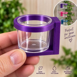 Könnte beinhalten: Eine violette, 3D-gedruckte magnetische Halterung mit einem klaren, zylindrischen Kunststoffbecher. Die Halterung verfügt über einen kreisförmigen Ring zur Befestigung des Bechers und eine flache, rechteckige Basis. Ein runder Einsatz zeigt weitere Farben.