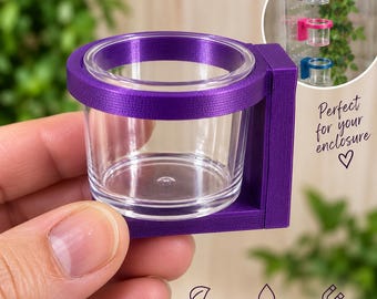 Könnte beinhalten: Eine violette, 3D-gedruckte magnetische Halterung mit einem klaren, zylindrischen Kunststoffbecher. Die Halterung verfügt über einen kreisförmigen Ring zur Befestigung des Bechers und eine flache, rechteckige Basis. Ein runder Einsatz zeigt weitere Farben.