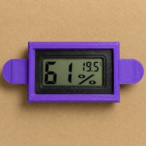 Op de afbeelding: Een paarse digitale hygrometer en thermometer met een rechthoekig frame en zijlipjes. Het zwarte scherm toont de tekst 61% en 19.5°C in een duidelijk digitaal lettertype, wat de huidige vochtigheids- en temperatuurniveaus aangeeft.