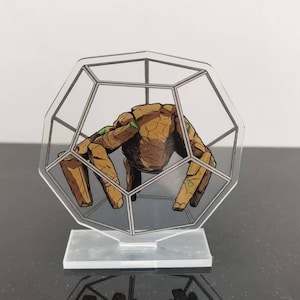 May include: A clear acrylic figurine featuring a brown, rock-like creature inside a geometric cage. The creature has green accents and is mounted on a clear base. The design is a unique decorative item.
