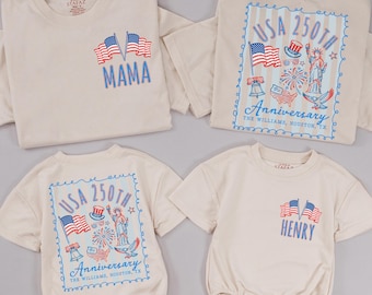 Pode incluir: Quatro camisetas e macacões creme com designs patrióticos. Uma camisa diz "MAMA" com bandeiras americanas. Outra apresenta "USA 250th Anniversary" com a Estátua da Liberdade. Um macacão diz "HENRY" com bandeiras.