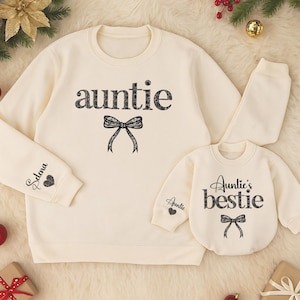 May include: Cream-colored matching aunt and niece sweatshirts. The adult sweatshirt has the word "auntie" and a bow graphic. The child's sweatshirt says "Auntie's bestie" with a bow. The aunt's sleeve has a name and heart graphic.