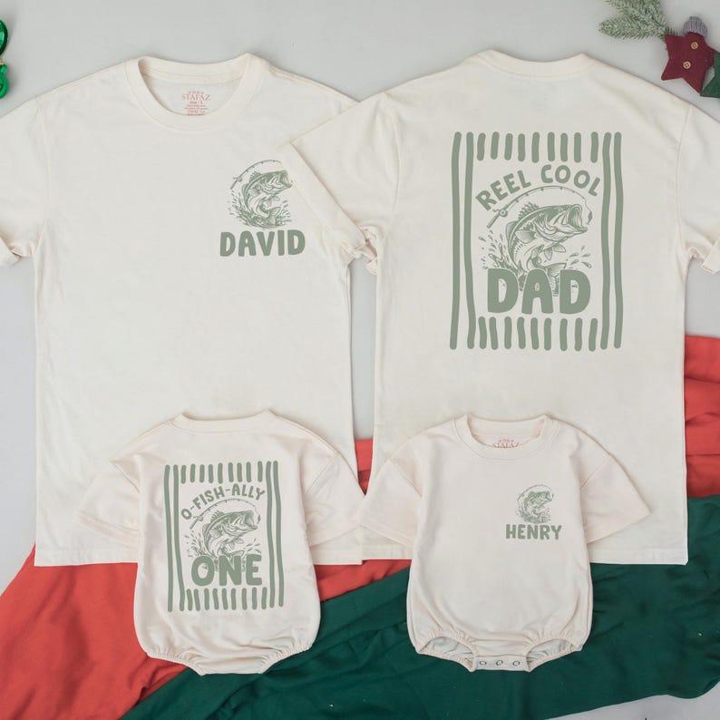 Puede incluir: Dos camisetas y dos bodies de beb&eacute; color blanco hueso con gr&aacute;ficos en verde salvia. Las camisetas de adulto tienen un gr&aacute;fico de pez con el texto DAVID o REEL COOL DAD. Los bodies tienen un gr&aacute;fico de pez con O-FISH-ALLY ONE o HENRY.