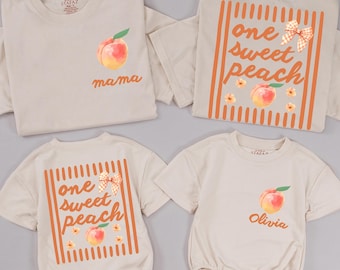 May include: Four beige garments including two t-shirts and two baby rompers. The designs feature orange striped frames, peach illustrations, gingham bows, and the text "one sweet peach," "mama," and "Olivia" in a cursive orange font.