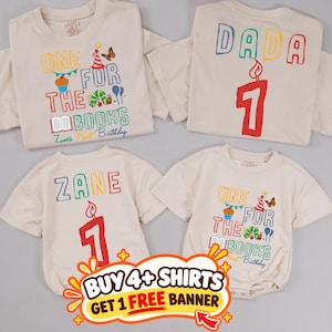 May include: Four beige t-shirts and bodysuits featuring colorful graphics. Designs include the text "ONE FOR THE BOOKS" with a caterpillar, cupcake, and butterfly, or "DADA" and "ZANE" above a large red number "1" candle graphic.