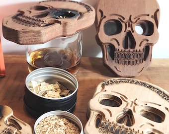 May include: A selection of wooden skull-shaped items, including coasters and decorative pieces, alongside a bottle of Glenfiddich Reserva 21 whisky. The skulls have detailed carvings and are displayed with small containers of wood chips.