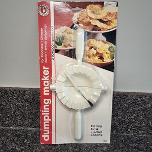 May include: A white plastic Rowoco dumpling maker in its original packaging. The tool features a circular press with a crimped edge and two handles. The packaging includes the text "dumpling maker," "For Japanese, Chinese, Italian, Jewish dumplings," and "A ROWOCO quality tool."