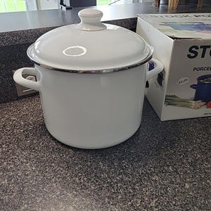 May include: A white enamel stock pot with a lid and silver trim. The pot has two side handles and a knob on the lid. A box with the words "STOCK POT" is visible in the background.