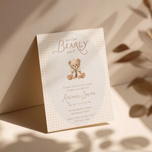 May include: A rectangular baby shower invitation card featuring a light beige gingham pattern border. The center oval contains a brown teddy bear illustration with a cream ribbon, and text reading We Can Bearly Wait, honoring Rachael Smith.