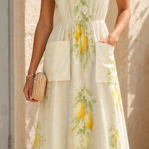 May include: A sleeveless midi dress in a light cream color featuring a repeating pattern of yellow lemons and green leaves. The dress has a V-neckline, a cinched elastic waist, and two large patch pockets on the front skirt section.