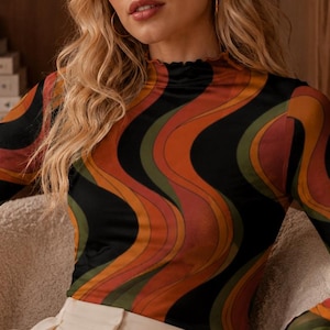 May include: A long-sleeve mock neck top featuring a wavy, multi-colored pattern in shades of black, orange, and olive green, paired with high-waisted cream-colored trousers that have a visible front pleat and a button closure at the waist.