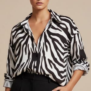 Pode incluir: Uma camisa com estampa de zebra em preto e branco com mangas compridas e gola. A camisa é combinada com calças pretas. A modelo está usando a camisa e as calças.