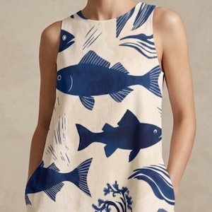 Peut inclure: Robe sans manches, longueur genou, avec un fond crème et un motif répétitif de poissons bleus. La robe a une silhouette simple en forme de A et présente une encolure ronde. Les illustrations de poissons varient en taille et en style, créant un thème aquatique fantaisiste.