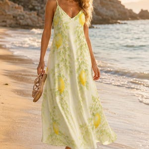 Puede incluir: Un vestido largo sin mangas de tono amarillo p&aacute;lido, con un patr&oacute;n repetitivo de limones de color amarillo brillante y ramas verdes con peque&ntilde;as flores blancas. La prenda tiene tirantes finos y un escote en forma de V.