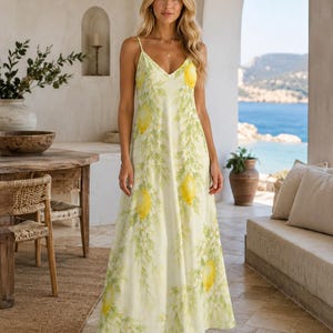 Puede incluir: Un vestido largo sin mangas con fondo amarillo claro y un patr&oacute;n repetitivo de limones amarillo brillante y ramas con hojas verdes. El vestido tiene un escote en V y tirantes finos, con una ca&iacute;da en silueta recta.