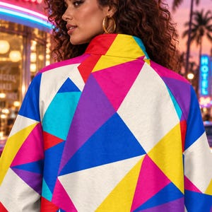 Puede incluir: Una chaqueta de cuello alto con un vibrante patr&oacute;n geom&eacute;trico de tri&aacute;ngulos en tonos amarillo brillante, azul real, magenta, morado y blanco. La prenda tiene mangas largas y un corte estructurado que muestra un dise&ntilde;o abstracto multicolor y llamativo.