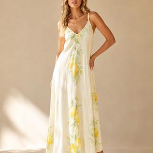 A woman stands facing forward in a light yellow maxi dress with a lemon and leaf print.