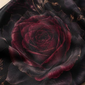 Puede incluir: Una tela negra con un estampado grande y detallado de una rosa color burdeos intenso en plena floraci&oacute;n. El dise&ntilde;o floral muestra intrincadas capas de p&eacute;talos con sombras oscuras y reflejos sutiles, creando una apariencia realista.