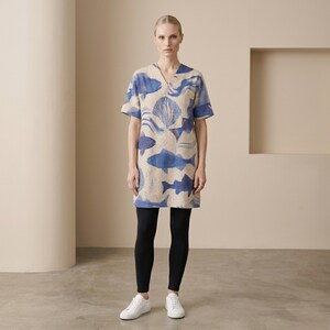Puede incluir: Vestido beige y azul con cuello en V con un estampado de vida marina, incluyendo peces y conchas. El vestido tiene mangas cortas y se usa con leggings negros y zapatillas blancas.