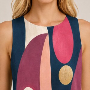 May include: A sleeveless top featuring a bold abstract pattern with deep navy blue, vibrant magenta, soft peach, and cream shapes. The design includes a prominent gold circular accent and a smaller white circle with a dark center on a smooth fabric.