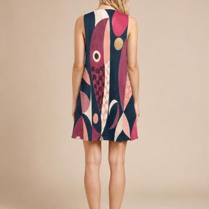 May include: A sleeveless mini dress featuring a dark navy blue background with a large, abstract graphic print of fish shapes in shades of magenta, light pink, and cream, accented with small circular gold details and a scale-like pattern.