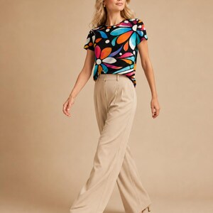 May include: A short-sleeved t-shirt featuring a black background with a vibrant, multi-colored floral pattern in shades of orange, pink, blue, and white, paired with high-waisted, wide-leg beige trousers that feature a pleated front detail.
