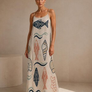 May include: A floor-length beige sleeveless dress with thin spaghetti straps, featuring a repeating pattern of dark blue fish, peach-colored fish, and various seashells, along with wavy lines in muted blue and green tones printed on the fabric.
