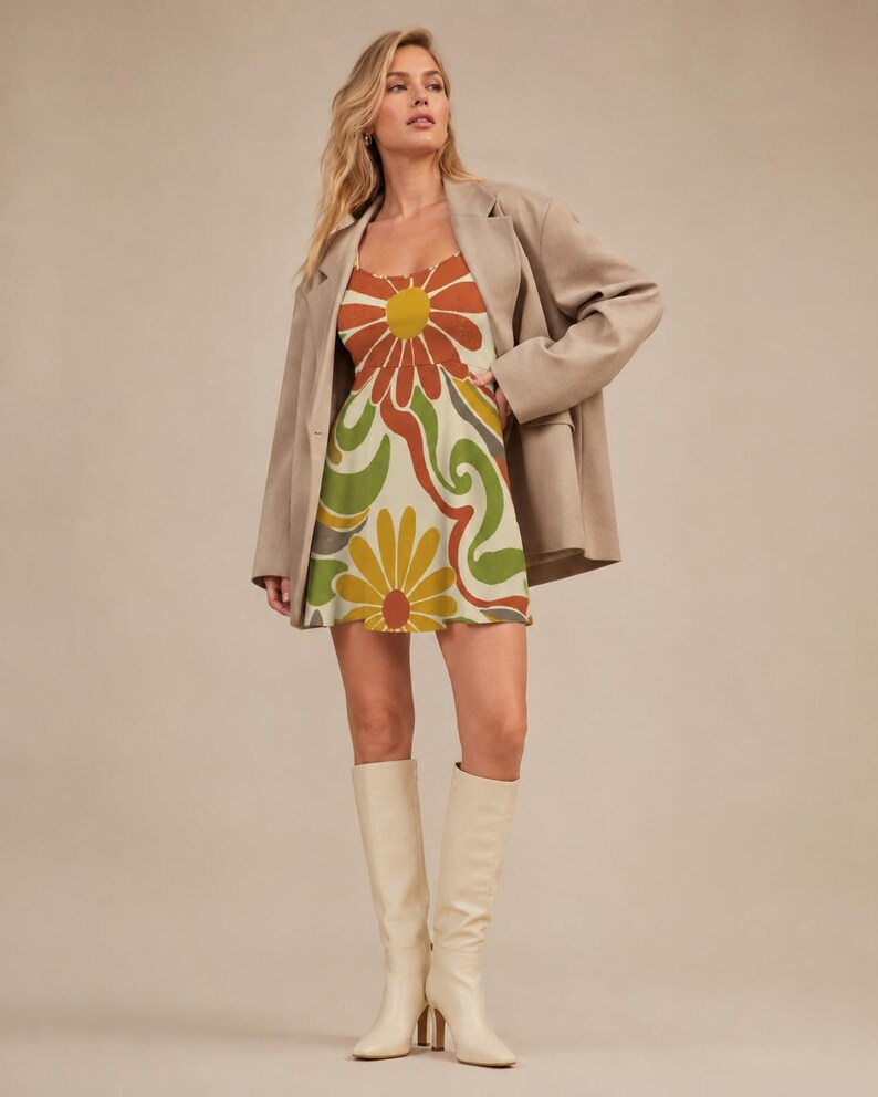 May include: A sleeveless mini dress featuring a large-scale floral and swirling abstract pattern in shades of orange, yellow, olive green, and cream, worn under an oversized beige blazer with long sleeves and white knee-high boots.