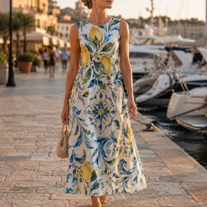 May include: A sleeveless midi dress featuring a white base with a vibrant print of yellow lemons, green leaves, and blue and yellow ornate scrollwork patterns. The dress has a round neckline and a straight, flowing silhouette that falls below the knee.
