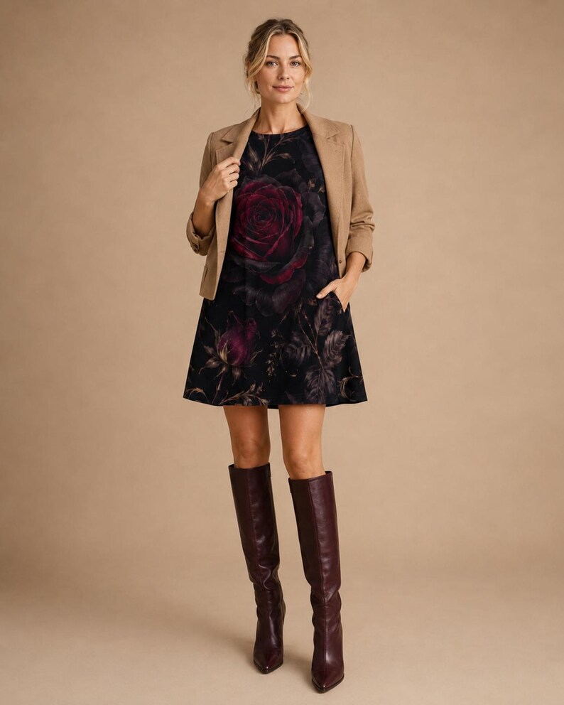 Puede incluir: Un vestido corto negro sin mangas con un estampado de una gran rosa de color rojo oscuro, usado bajo un blazer color canela con mangas tres cuartos. El conjunto se combina con botas altas de cuero color burdeos oscuro con punta fina.