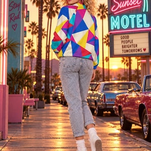 Puede incluir: Una chaqueta de manga larga con un patr&oacute;n geom&eacute;trico vibrante en tonos azul, amarillo, rosa y morado, combinada con pantalones vaqueros de mezclilla lavada al &aacute;cido, calcetines blancos y zapatillas blancas. La chaqueta tiene cuello y cremallera.