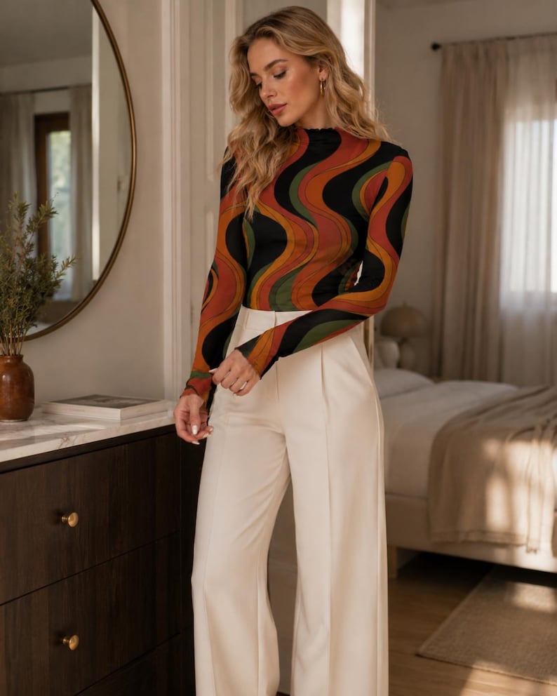 May include: A long-sleeved mock neck top featuring a wavy, multi-colored pattern in black, burnt orange, and olive green, paired with high-waisted, wide-leg trousers in a solid cream color with a front center crease.