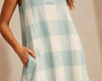 May include: A sleeveless, light blue and white checkered dress with a small fish emblem near the neckline and a leaf emblem near the pocket. The dress has a relaxed fit and a scoop neckline.