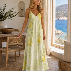 Puede incluir: Un vestido largo sin mangas con una base de color amarillo claro y un patr&oacute;n repetitivo de limones amarillo brillante y ramas de hojas verde suave. El vestido tiene un escote en V y tirantes finos, con una silueta recta hasta el suelo.