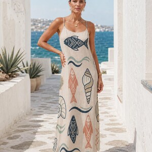 May include: A beige maxi dress featuring thin spaghetti straps and a scoop neckline. The fabric is decorated with a repeating pattern of stylized fish, seashells, and wavy lines in shades of dark blue, muted orange, and soft green throughout.