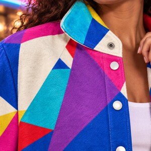 Puede incluir: Una chaqueta con un vibrante patr&oacute;n geom&eacute;trico de tri&aacute;ngulos en tonos rosa brillante, morado, azul real, cian, amarillo y blanco roto. La prenda cuenta con un cuello vuelto y una tapeta frontal con botones de presi&oacute;n de color plateado.