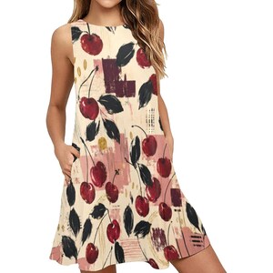 A woman wearing a sleeveless cream A-line mini dress with a red and black cherry print and pockets, with her hands in the pockets.