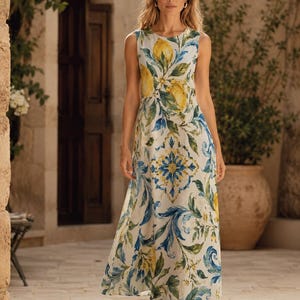 May include: A sleeveless floor-length dress featuring a white base with a vibrant print of yellow lemons, green leaves, and blue swirling floral patterns. The garment has a round neckline and a fitted bodice that flows into a relaxed skirt.