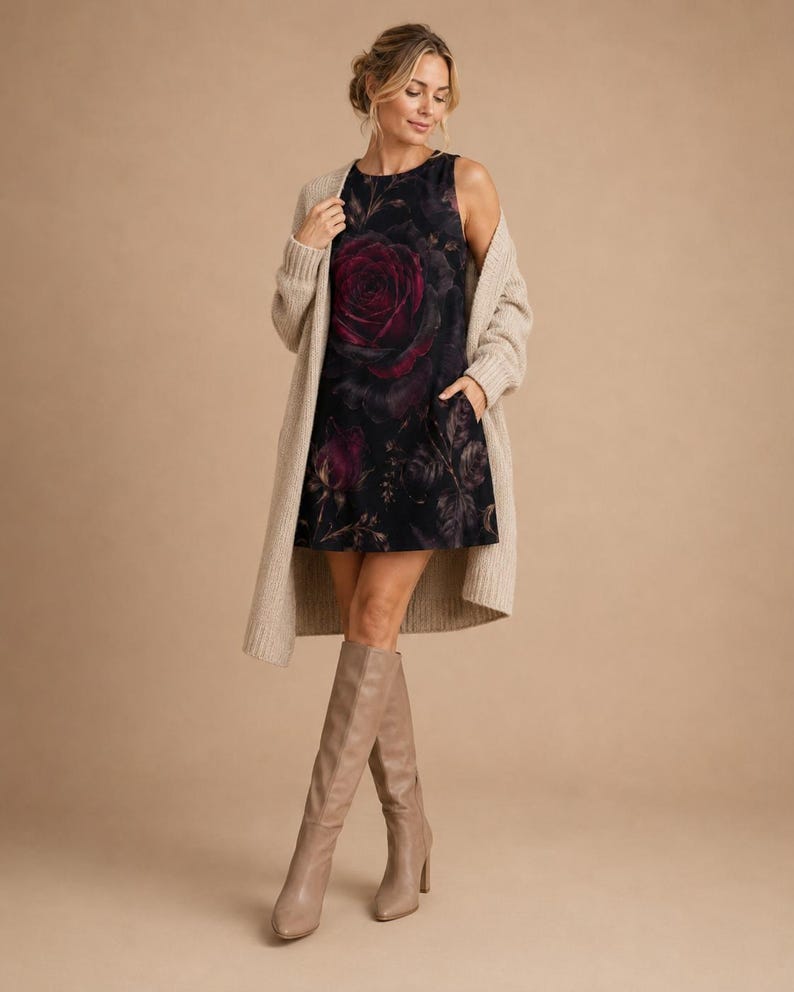 Puede incluir: Un vestido corto sin mangas de color negro con un estampado de rosas grandes en rojo oscuro, combinado con un c&aacute;rdigan largo de punto acanalado en color beige y botas altas de cuero beige. El vestido tiene cuello redondo y bolsillos laterales.