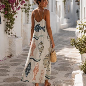 May include: A sleeveless, floor-length beige maxi dress featuring a repeating pattern of stylized fish, seashells, and wavy lines in shades of blue, orange, and green. The dress has thin spaghetti straps and a low-cut back design.