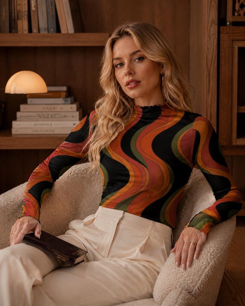 May include: A long-sleeve mock neck top featuring a wavy, multi-colored pattern in shades of black, orange, and olive green, paired with high-waisted cream-colored trousers that have a visible front pleat and a button closure at the waist.