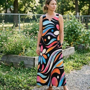 May include: A sleeveless maxi dress with a black background and a vibrant, colorful abstract design. The pattern includes flowing lines and shapes in shades of blue, orange, pink, and white. The dress has a V-neckline and a floral design on the front.