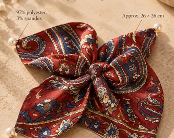 Könnte beinhalten: Ein quadratisches Satin-Accessoire mit einem Paisley-Muster in Rot, Blau und Gold, verziert mit einer Perle an jeder Ecke. Der Stoff besteht aus 97% Polyester und 3% Elasthan und misst ca. 26 x 26 cm. Text: Pearl-Trimmed Satin, Soft faux-silk feel.