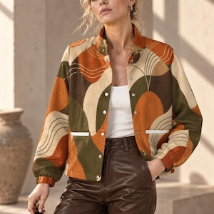 May include: A long-sleeve jacket featuring a multi-colored abstract pattern in shades of burnt orange, olive green, and cream. The jacket has a stand-up collar, silver-tone snap button closures, and two front pockets with white trim, worn over a white top.