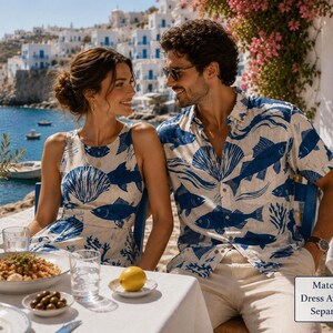 A man and woman in matching fish-print outfits sit at an outdoor table with food and drinks, overlooking a coastal town.