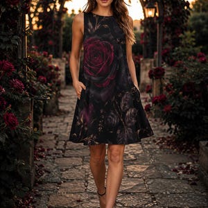 Puede incluir: Un vestido negro sin mangas hasta la rodilla con un estampado grande de rosas rojo oscuro y follaje verde. El vestido tiene un cuello redondo, una silueta en forma de A relajada y bolsillos laterales visibles integrados en las costuras.