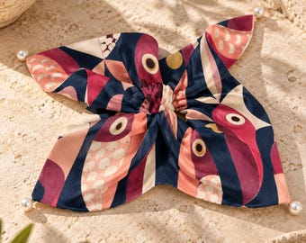 May include: A square silk scarf featuring a repeating pattern of stylized birds in shades of navy blue, magenta, and soft pink. The scarf is gathered at the center and finished with four small white pearl beads attached to each of the four corners.