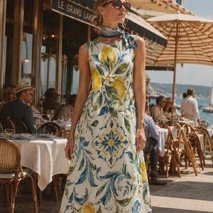 May include: A sleeveless midi dress featuring a white base with a vibrant print of yellow lemons, green leaves, and blue and yellow decorative tile patterns. The dress has a round neckline and is paired with a matching patterned neck scarf.
